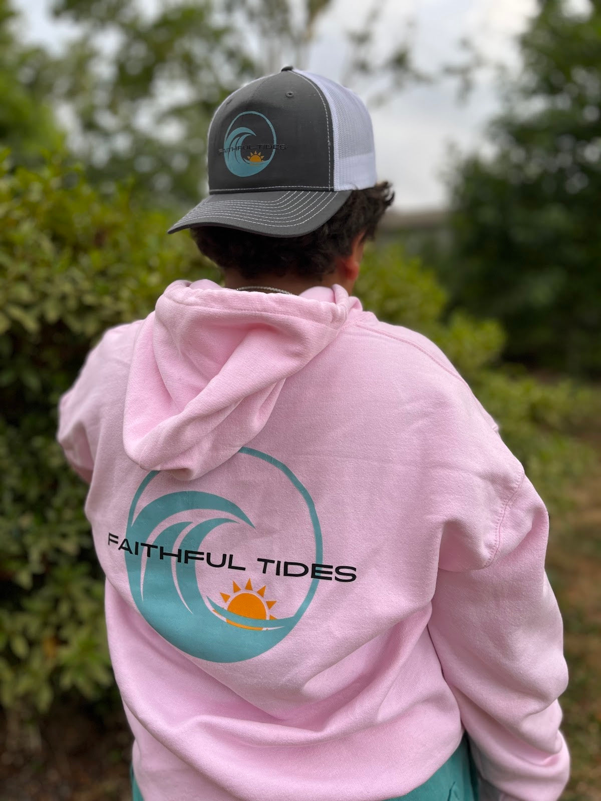 Customer outdoors wearing a pink hoodie with a large Faithful Tides transfer